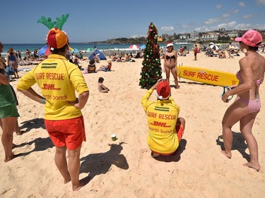 A surf lifesaver (C) takes a photo for a visitor (in background) posing next to a Christmas tree on Bondi Beach to mark Christmas Day in Sydney on December 25, 2016.