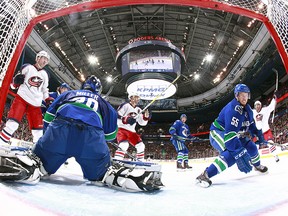 Alex Biega of the Canucks turns to the goal as Brandon Saad of the Blue Jackets (right) celebrates after scoring on Ryan Miller.