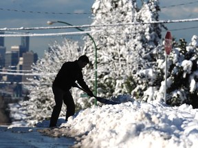 A man shovels snow on Capitol Hill with the Vancouver skyline in the background in Burnaby, BC., December 6, 2016.