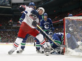 Ben Hutton of the Canucks grabs Boone Jenner of the Blue Jackets as Ryan Miller reaches for the puck.