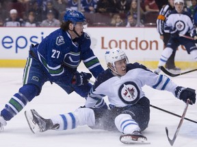 Vancouver Canucks defenceman Ben Hutton (27) fights for control of the puck with Winnipeg Jets right wing Patrik Laine.