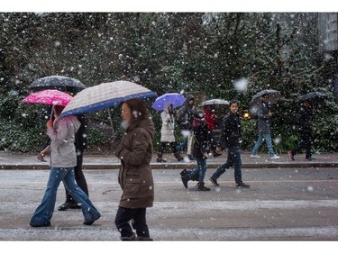 Pedestrians carrying umbrellas walk along Robson St. as snow falls in downtown Vancouver, B.C., on Monday December 5, 2016. Environment Canada has issued a snowfall warning for Metro Vancouver.