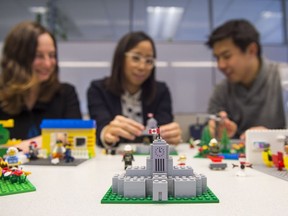 A Vancouver City Hall made of Lego sits on a table as, from left, Amanda Gibbs, Jhenifer Pabillano and Lihwen Hsu of the City of Vancouver Public Engagement Team build other Lego structures in Vancouver on Dec. 9.