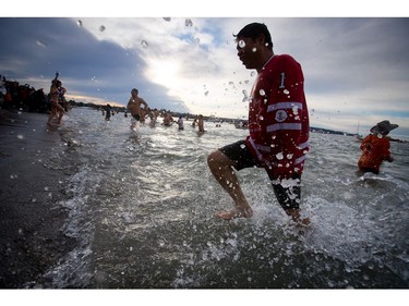 Participants are silhouetted while running in and out of the frigid waters of English Bay during the Polar Bear Swim in Vancouver, B.C., on Sunday, January 1, 2017. The event, hosted by the Vancouver Polar Bear Swim Club, was first held on new year's day in 1920.