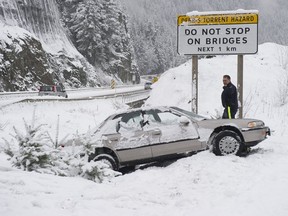 A Squamish, BC RCMP member inspects a car in the ditch along the Sea-to-Sky highway north of Lions Bay Friday, January 6, 2017.