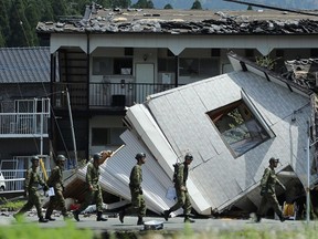 Soldiers walk before a collapsed house to search for missing people in Minami-Aso, Kumamoto preficture, on April 22, 2016.