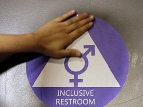 FILE - In this May 17, 2016 file photo, a new sticker is placed on the door at the ceremonial opening of a gender neutral bathroom at Nathan Hale High School in Seattle. A government official says the Trump administration will revoke guidelines that say transgender students should be allowed to use bathrooms and locker rooms matching their chosen gender identity. (AP Photo/Elaine Thompson, File)