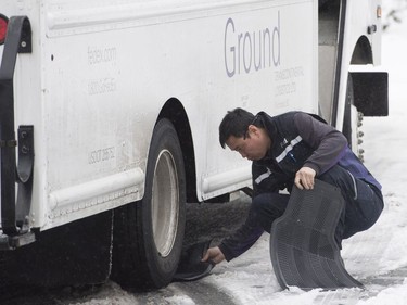 A delivery man uses floor matts from his truck to try and free his vehicle on a small snow covered hill in North Vancouver, B.C., Friday, Feb. 3, 2017. Heavy snow hit the northshore leaving cars and trucks slipping and sliding.