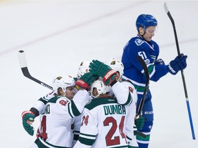 Minnesota Wild's Mikael Granlund, of Finland, from left, Marco Scandella, Matt Dumba and Mikko Koivu, of Finland, celebrate Granlund's second goal as Vancouver Canucks' Troy Stecher, back right, skates to the bench during second period NHL hockey action, in Vancouver on Saturday, February 4, 2017.