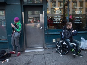 A woman, left, prepares to inject herself with an unknown substance as a man sits in a wheelchair outside Insite, the supervised consumption site, in the Downtown Eastside of Vancouver, B.C., on Tuesday, February 21, 2017.