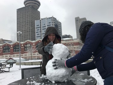 Students Natalia Joya (left) and Dana Angel build their first snowman at Granville Square Plaza. Vancouver was hit with a snowfall warning Friday. Environment Canada was calling for as much as 20 cm to fall by Saturday morning.