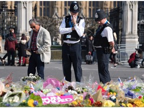 Police officers stop to look at floral tributes to the victims of the March 22 terror attack, near the Houses of Parliament in Westminster, central London on March 27, 2017. British police investigating a deadly attack on parliament made a new arrest Sunday as officials set their sights on accessing WhatsApp, the heavily-encrypted messaging service that was used by the killer.