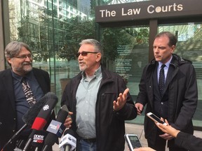 David Trapp, centre, who is the representative plaintiff in a class-action lawsuit aimed at stopping partisan B.C. government advertising, talks to reporters outside the Vancouver Law Courts on Monday. His lawyers, David Fai, with beard, and Paul Doroshenko stand by his side.