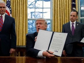 FILE - In this Jan. 23, 2017, file photo, Vice President Mike Pence, left, and White House Chief of Staff Reince Priebus, right, watch as President Donald Trump shows off an executive order to withdraw the U.S. from the 12-nation Trans-Pacific Partnership trade pact agreed to under the Obama administration, in the Oval Office of the White House in Washington. Trump campaigned on an ‚ÄúAmerica First‚Äù trade policy of bracing clarity: Renegotiate or abandon NAFTA and crack down on China‚Äôs trade