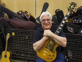 Dr Barry Rich. holds a Gibson electric guitar beside bins of his other guitars waiting for auction at Able Auctions Surrey on May 7.