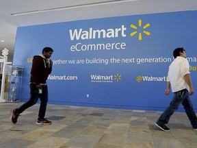 FILE - In this Wednesday, Sept. 18, 2013, file photo, two Wal-Mart employees walk past a sign in the lobby at the Walmart.com office in San Bruno, Calif. Wal-Mart‚Äôs acquisition of Jet.com is accelerating its progress in e-commerce as it works to narrow the gap between itself and online leader Amazon. Wal-Mart is betting its online future on essentials like produce and groceries and has adjusted its shipping strategy. But Amazon keeps innovating too. (AP Photo/Jeff Chiu, File)