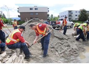 Trent Johnston, left, crew leader with B.C. Forestry firefighters, holds a sandbag open while Kit Nilsson shovels sand into the bag in Kelowna on Sunday afternoon.