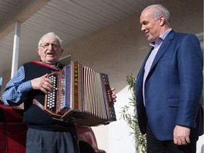 B.C. NDP Leader John Horgan listens as local resident Tony Zelko plays a squeezebox and sings "You Are My Sunshine" outside his home where Horgan's campaign bus had stopped to take a woman to an advance polling station to vote, in Osoyoos on Saturday.