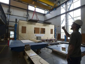 Pictured is a reproduction of a quake-retrofitted, wood-frame school building, built on a hydraulic shake table, inside the University of B.C. Earthquake Engineering Research Facility. It was put through several simulated earthquakes Wednesday. Martin Turek, UBC engineering manager, is gesturing to the control room.