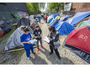 From the left, Joyce, Crystal Cardinal and Gina Baptis read the 'notice served' at their Main Street homeless camp. The city served notice on Tuesday for them to leave the property in Vancouver.