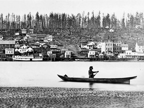 1866 photo of a First Nations man paddling his canoe in front of the fledgling city of New Westminster.