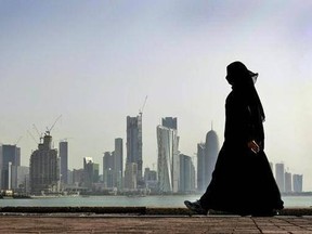 FILE- In this May 14, 2010 file photo, a Qatari woman walks in front of the city skyline in Doha, Qatar. Qatar likely faces a deadline this weekend to comply with a list of demands issued to it by Arab nations that have cut diplomatic ties to the energy-rich country, though its leaders already have dismissed the ultimatum. (AP Photo/Kamran Jebreili, File)