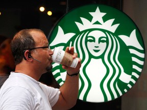 A man drinks a beverage in front of the Starbucks logo.