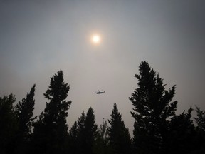 In this July 8, 2017 photo, smoke obscures the sun as a helicopter carrying a bucket battles the Gustafsen wildfire near 100 Mile House, B.C.