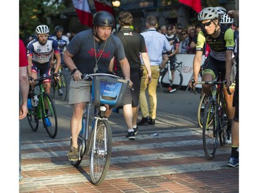 A man on a Mobi rental bike rides through the mens competitors prior to the Men's 50 lap / 60 km Global Relay Gastown Grand Prix , Vancouver, July 12 2017.