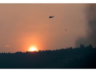 As the sun sets a helicopter prepares to dump water on a blaze near Williams Lake, BC Wednesday, July 12, 2017. The residents of Williams Lake are on alert for possible evacuation due to raging wildfires in the region.