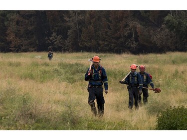 Fire fighters from the Alkali Lake Indian Band walk through a field after putting out hot spots near Alexandria, BC after the Soda Creek Fire jumped across the Fraser River, July, 16, 2017.
