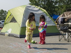 Domica Shaw watches her sister Taya play hopscotch in the parking lot of the College of New Caledonia in Prince George where the family has been camping for over a week after fleeing wildfires in the Williams Lake area.