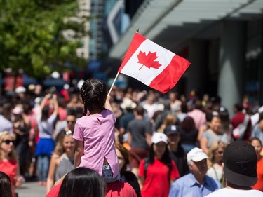 A young girl waves a Canadian flag while being carried through the crowd during Canada Day celebrations in Vancouver, B.C., on Saturday, July 1, 2017. THE CANADIAN PRESS/Darryl Dyck