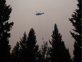 A helicopter carrying a bucket battles the Gustafsen wildfire near 100 Mile House. The B.C Wildfire Service and the Canadian Armed Forces would both like to base their aircraft out of the Kamloops Airport but can't until the smoke clears.