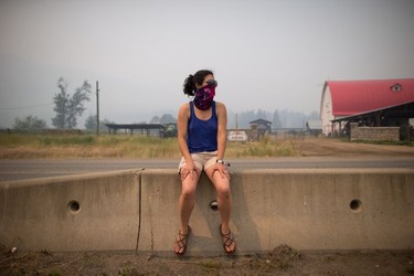 Luana Avila wears a bandana over her face because of smoke and ash in the air from wildfires as she waits for her children at gas station in Little Fort, B.C., on Saturday July 8, 2017. Avila and her husband, from Vancouver, were waiting for his parents to drop off their kids who were staying with them in 100 Mile House.