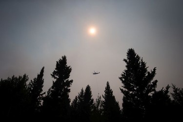 Smoke obscures the sun as a helicopter carrying a bucket battles the Gustafsen wildfire near 100 Mile House, B.C., on Saturday July 8, 2017.