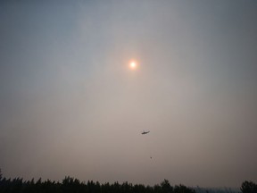 Smoke obscures the sun as a helicopter carrying a bucket battles the Gustafsen wildfire near 100 Mile House.