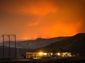 A wildfire burns on a mountain in the distance east of Cache Creek behind a house in Boston Flats, B.C., in the early morning hours of Monday July 10, 2017.