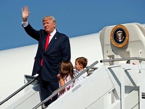 FILE- In this Aug. 4, 2017, file photo, President Donald Trump waves as he walks down the steps of Air Force One with his grandchildren, Arabella Kushner, center, and Joseph Kushner, right, after arriving at Morristown Municipal Airport to begin his summer vacation at his Bedminster golf club in Morristown, N.J. The president has decamped from Washington to his private golf club in central New Jersey. But he has repeatedly pushed back on the idea that this is a relaxing August getaway. (AP Photo