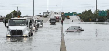 A man walks down the median as trucks navigate floodwaters from Tropical Storm Harvey along Interstate 610 Sunday, Aug. 27, 2017, in Houston, Texas.