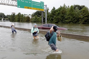 Evacuees wade down a flooded section of Interstate 610 as floodwaters from Tropical Storm Harvey rise Sunday, Aug. 27, 2017, in Houston, Texas.