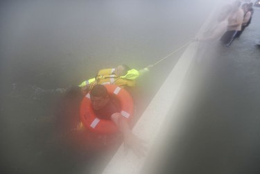 Wilford Martinez, bottom, grabs the median as he is rescued from his flooded car along Interstate 610 in floodwaters from Tropical Storm Harvey on Sunday, Aug. 27, 2017, in Houston, Texas.