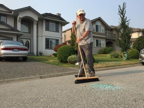 Andy Daniel sweeps up glass on the street in front of his house in the 15900-block 89A Avenue in Surrey, where a shooting took place around 10:30 p.m. on Tuesday.