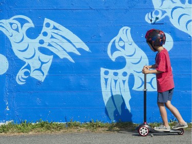 A boy rides past a mural by Khelsilem at the Vancouver Mural Festival.