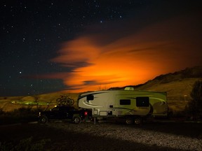 A trailer parked at a campground in Savona, B.C., is seen as the Elephant Hill wildfire burns in the distance near Clinton, illuminating smoke in the sky during the early morning hours of Sunday July 30, 2017.