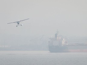 Smoke from wildfires burning in central British Columbia hangs in the air as a seaplane prepares to land on the harbour near the bulk carrier Nanakura, in Vancouver on Aug. 10.