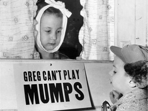 In this Jan. 16, 1957 file photo, Jon Douglas, 6, right, visits his friend, Greg Cox, standing behind a sign warning he has mumps, on the door of his home in Altamont, Ill. Fifty years ago, mumps was once a childhood rite of passage of puffy cheeks and swollen jaws. That all changed with the arrival of a vaccine in the late 1960s, and mumps nearly disappeared.