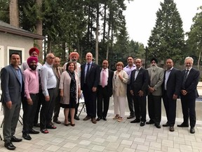 Premier John Horgan (centre) and Surrey Mayor Linda Hepner (second to the right of Horgan, in beige and white pantsuit) poses with others, including convicted gunman Maninder Gill (third to the left of the premier).