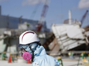 In this Feb. 10, 2016, file photo, a Tokyo Electric Power Co. (TEPCO) employee, wearing a protective suit and a mask, walks in front of the No. 1 reactor building at the tsunami-crippled Fukushima Dai-ichi nuclear power plant in Okuma, Fukushima Prefecture, northeastern Japan.