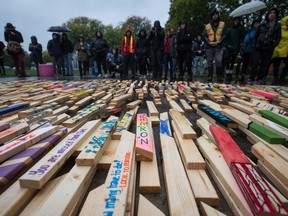 People listen to speeches on Sept. 29, 2017, as 2,224 wooden stakes representing the number of confirmed overdose deaths in B.C. over the last three years, many of them painted with names of overdose victims, are placed on the ground at Oppenheimer Park in Vancouver.